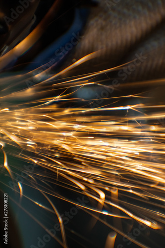 Worker cutting, grinding and polishing motorcycle metal part with sparks indoor workshop. Super macro close-up. 