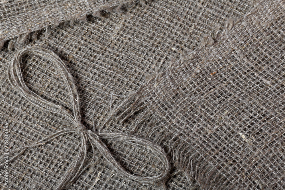 Fototapeta premium Coarse linen fabric. On it lies a bow of linen thread.