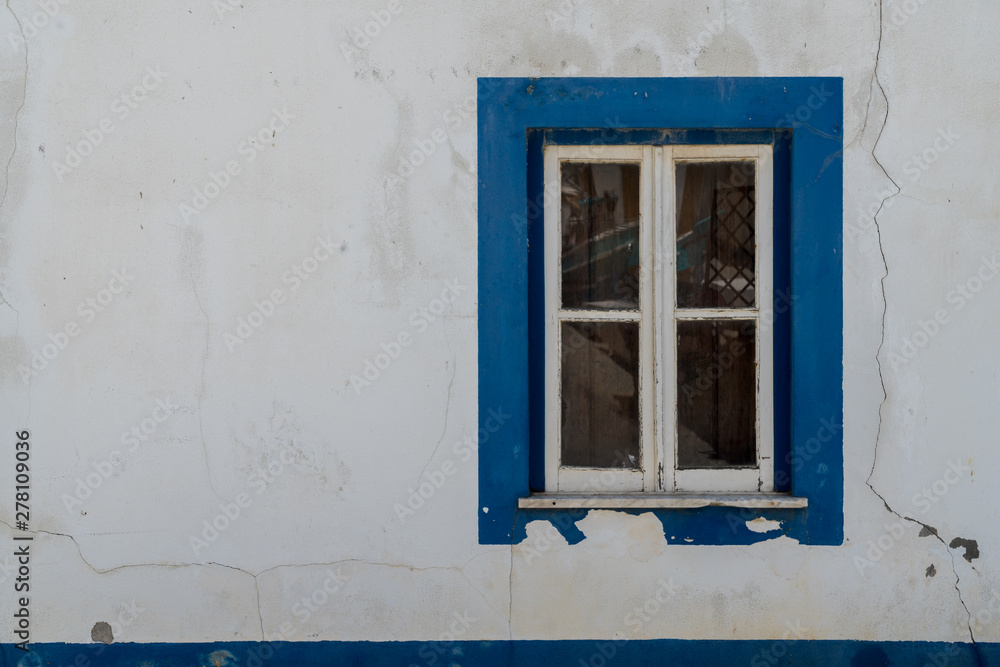 Window with glass shutters and blue details on the right side of a white clean wall.