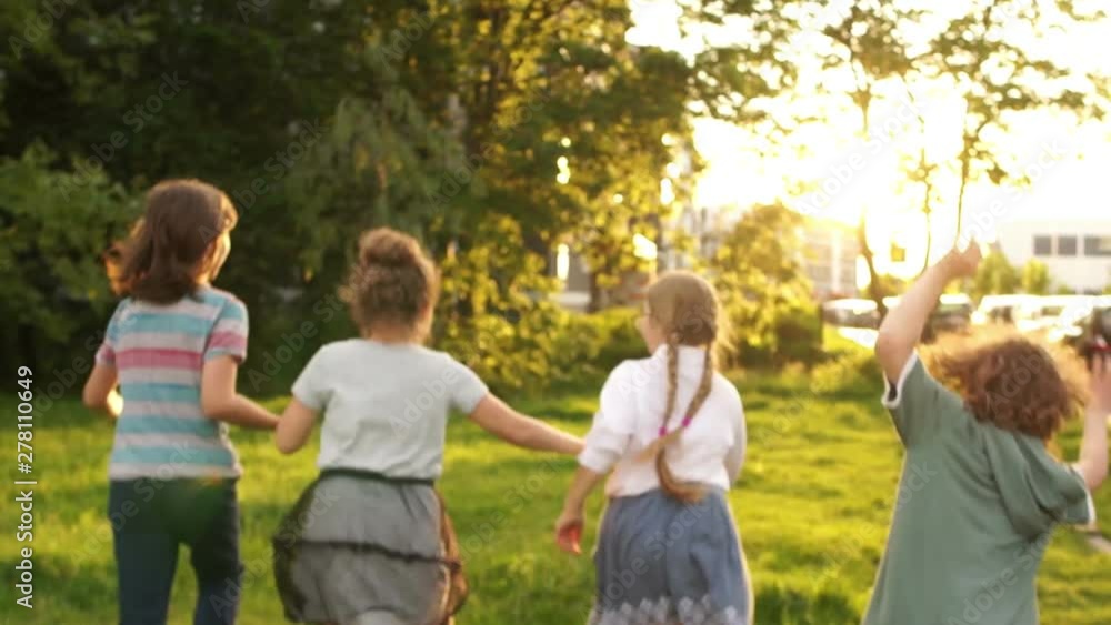 Children schoolchildren running into the distance on the background of green trees and sunset. The boy makes a flip on his hands. School friendship, back to school, lens flare
