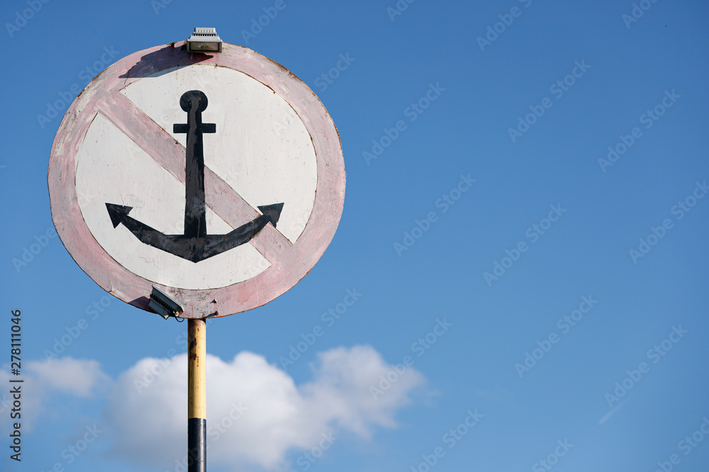 An old sign for ships indicating a parking ban in this place. Sign, do not throw anchors, against the blue sky.