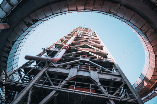 Wide-angle shot of a modern building of an oil refinery or a contemporary fuel factory facility in an industrial zone, with a round bridge around, many pipes, and iron beams, the clear sky behind photo