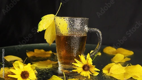 A transparent glass cup is wet in the rain of hot tea in the midst of an autumn landscape: yellowed fallen leaves, yellow flowers. autumn mood.