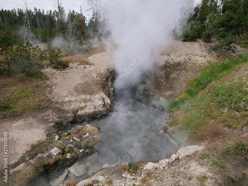 Wide view of the stunning Dragon's Mouth Spring, a turbulent hot spring with water sloshing in and out of the cavern at Yellowstone National Park.