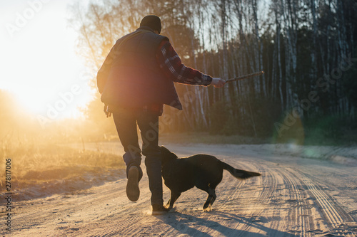 man with active happy black dog playing on the road forest park during sunset or sunrise