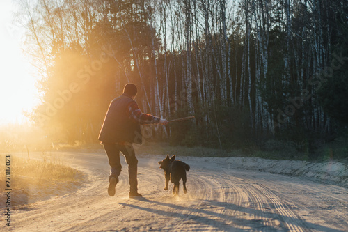 man with active happy black dog playing on the road forest park during sunset or sunrise