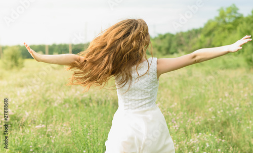 Beautiful and happy young girl running on the green field in a white dress
