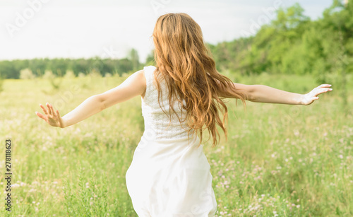 Beautiful and happy young girl running on the green field in a white dress