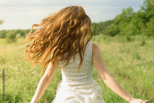 Beautiful and happy young girl running on the green field in a white dress