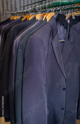 A rack of old suits and tuxedos on display for sell at charity recycling centre