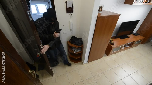 A masked burglar with gun in his hand is breaking into a home when suddenly a brave goodwife coming with her duster and fight back and finally she has managed to kick the intruder out of the house photo