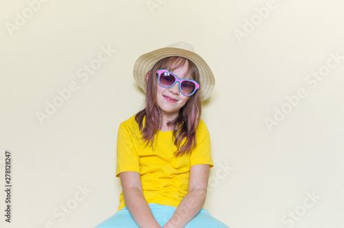 The child sits in the room on the floor emotion on his face. Little girl in a yellow T-shirt, glasses and a straw hat.