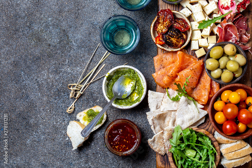 Antipasto. Wine set appetizer. Ham serrano  smoked salmon  dried and fresh tomatoes olive cheese  wine on board. Top view  gray cncrete background