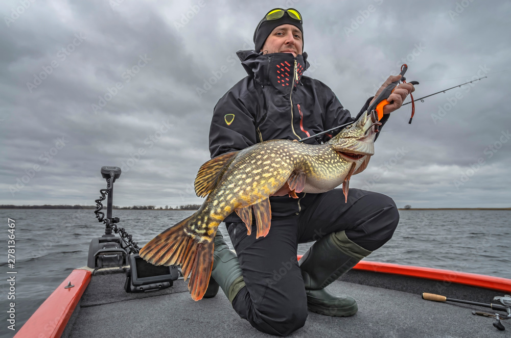 Pike fishing. Happy fisherman with big fish trophy at the boat with tackles