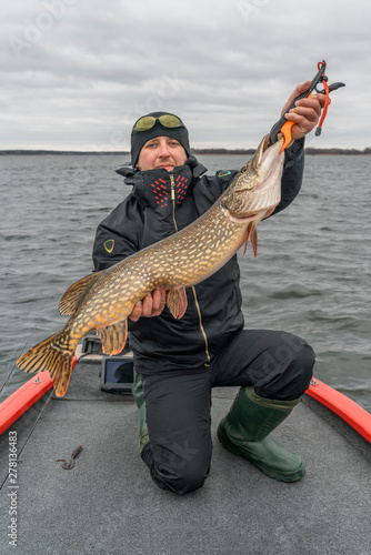 Pike fishing. Happy fisherman with big fish trophy at the boat with tackles