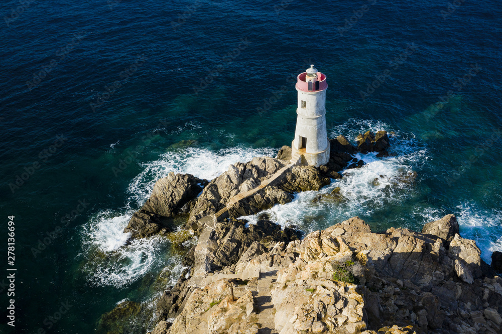 View from above, stunning aerial view of an old and beautiful lighthouse located on a rocky coast bathed by a rough sea. Faro di Capo Ferro, Porto Cervo, Sardinia, Italy.