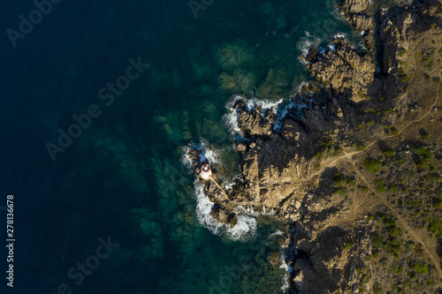 View from above, stunning aerial view of an old and beautiful lighthouse located on a rocky coast bathed by a rough sea. Faro di Capo Ferro, Porto Cervo, Sardinia, Italy.
