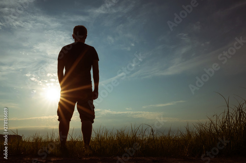 Silhouette of a young man against the backdrop of the setting sun and sky. The concept of loneliness, freedom, choice. Man of dense build in a t-shirt and shorts. Place for text, minimalism.