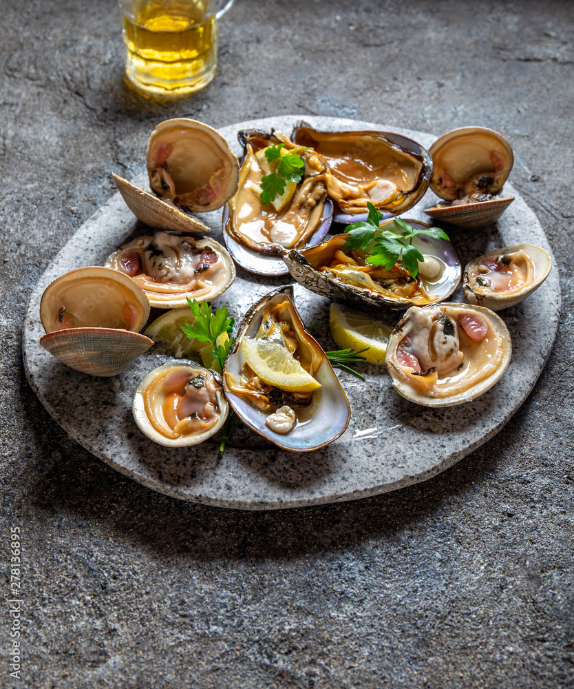 Raw seafood clams and mussels shellfish with lemon and cilantro on gray plate Raw seafood clams and mussels shellfish with lemon and cilantro on gray plate