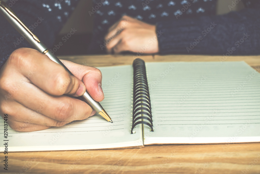 Woman wearing a blue sweater is writing a book. On a brown wood table. Woman wearing a blue sweater is writing a book. On a brown wood table.