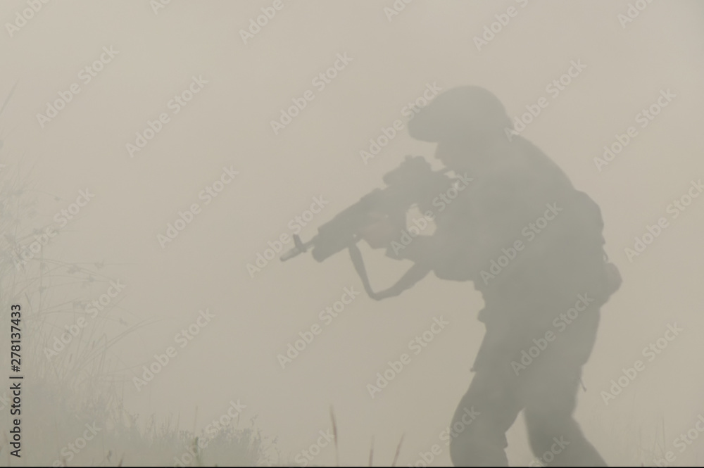 Military with a gun in his hands and in a helmet moves cautiously through the smoke and thickets - obrazy, fototapety, plakaty 