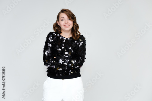 Portrait below the belt on a white background pretty young brunette woman in a black sweater and white trousers with glitters. Standing in different poses, talking, showing emotions.