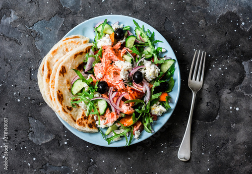 Healthy diet lunch - baked salmon, fresh vegetables, feta cheese salad on a dark background, top view