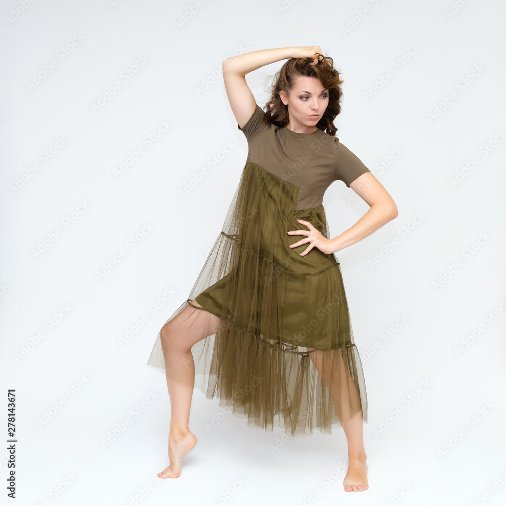 Fototapeta premium Portrait in full growth on a white background pretty young brunette woman in a green dress with beautiful hair. Standing in different poses, talking, showing hands, demonstrating emotions.