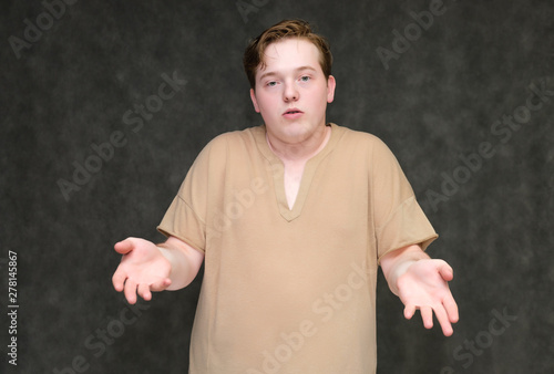 Portrait to the waist on a gray background of a handsome young man in a brown T-shirt. stands directly in front of the camera in various poses, talking, demonstrating emotions.