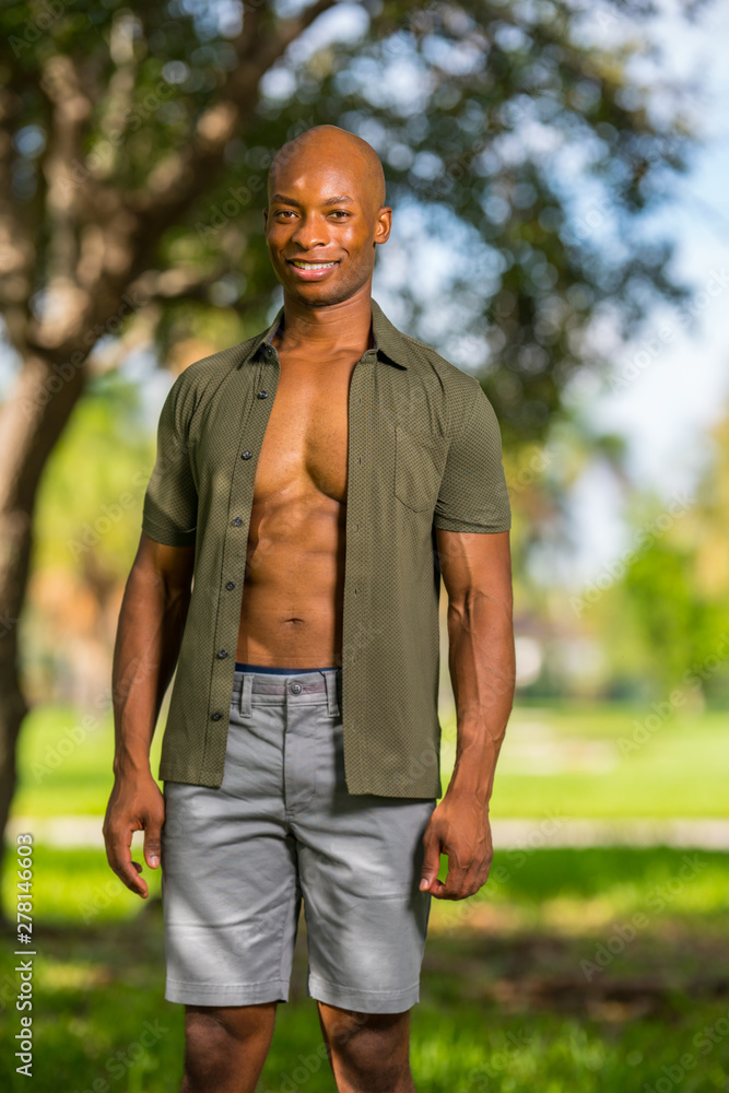 Photo of an attractive young bald black man smiling at camera. African American male model enjoying holiday in the park Photo of an attractive young bald black man smiling at camera. African American male model enjoying holiday in the park