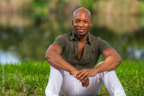 Portrait of a fashionable African American man sitting on grass in the park. Man is smiling and looking at camera