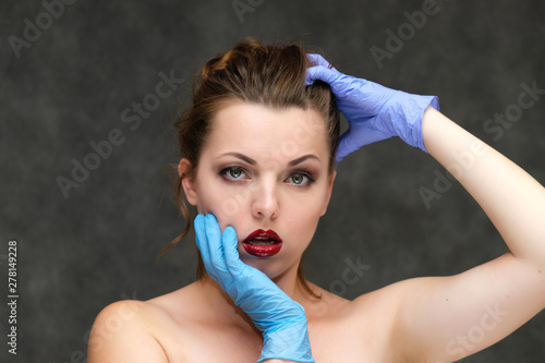 Close-up portrait on a gray background of a pretty young brunette woman with perfect skin of the face, in blue gloves. Beauty, great makeup. Talking with emotions.