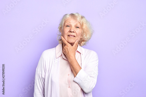 Old beautiful serious woman in uniform holding hand near chin thoughtfully looking at the camera over light blue background. close up portrait. idea, plan.