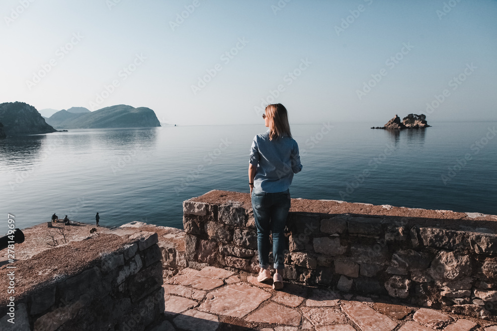 Back view of woman thinking alone and watching the sea with the horizon in the background, Montenegro. Back view of woman thinking alone and watching the sea with the horizon in the background, Montenegro.