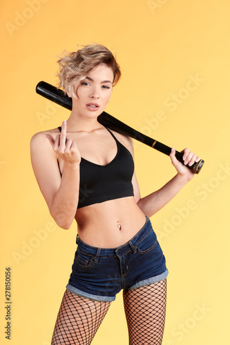 blonde attractive slim naughty girl with a bat showing her middle finger. close up portrait. isolated yellow background. studio shot © alfa27