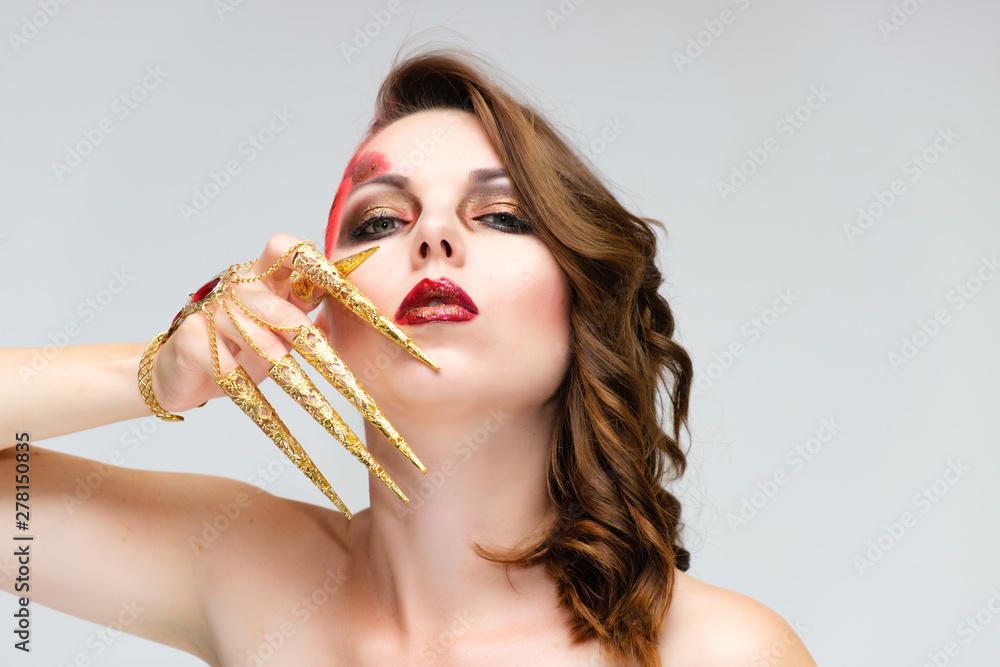 Close-up portrait on a white background of a pretty young brunette woman with beautiful makeup, with gold jewelry on her hand. Beauty, great makeup. Shows emotions.