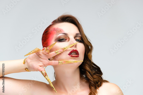 Close-up portrait on a white background of a pretty young brunette woman with beautiful makeup, with gold jewelry on her hand. Beauty, great makeup. Shows emotions.