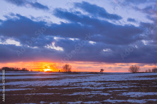 Sunset with orange sun in the clouds over snowy rural fields