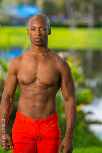 Portrait of a handsome shirtless fitness model posing in the park. Lit with off camera flash