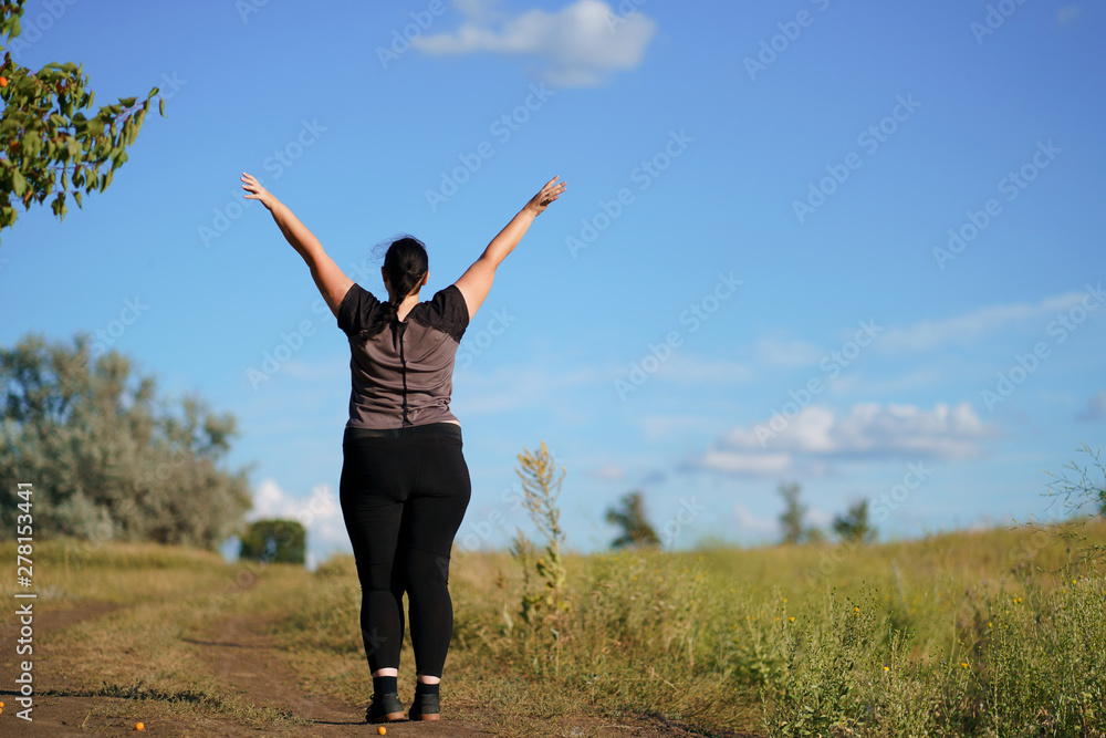 Body positive, confidence, high self esteem, free your mind concept. Overweight woman rising hands towards the sky, view from the back Body positive, confidence, high self esteem, free your mind concept. Overweight woman rising hands towards the sky, view from the back