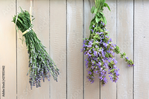 fresh lavender and fresh sage hanging in a bouquet on a white wooden wall to dry