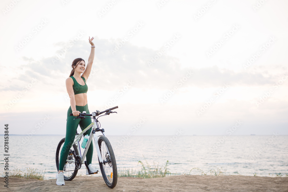 Beautiful young brunette woman resting after bicycle ride at sunrise. Model listening to music with wireless earbuds in the morning.