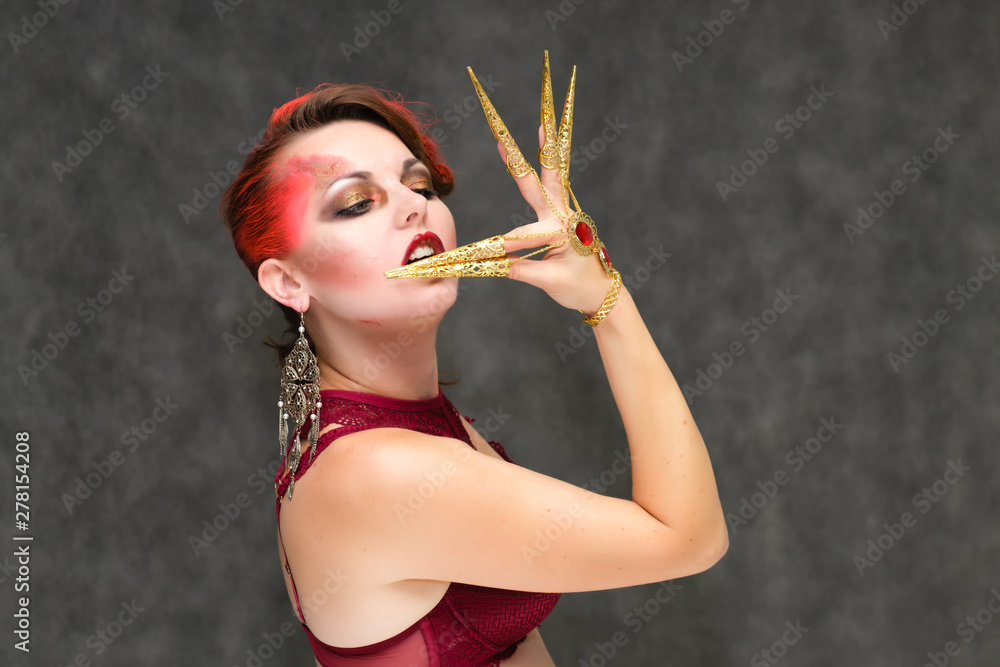 Obraz premium Portrait to the waist on a gray background of a pretty young brunette woman with beautiful makeup, with gold jewelry on her hand. Art, beauty, great makeup. Shows emotions.