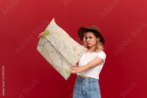 Thoughtful blond girl with curly hair in a white t-shirt and a sundown hat looks at the map trying to find itinerary while traveling. photo