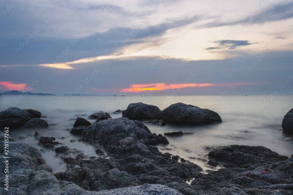 The shore of the calm sea of the Gulf of Thailand without people, waves shot on a long exposure. Large rocks in the foreground  