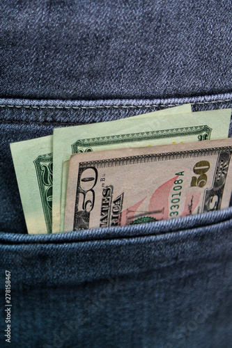 money, banknotes of 20 and 50 american dollars peeking out of the pocket of jeans, vertical photo