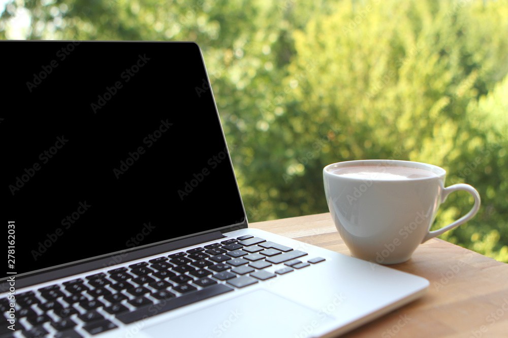 Mock up concept of remote work, downshifting using laptop with blank black desktop screen with a cup of coffee on a wooden table in nature Mock up concept of remote work, downshifting using laptop with blank black desktop screen with a cup of coffee on a wooden table in nature