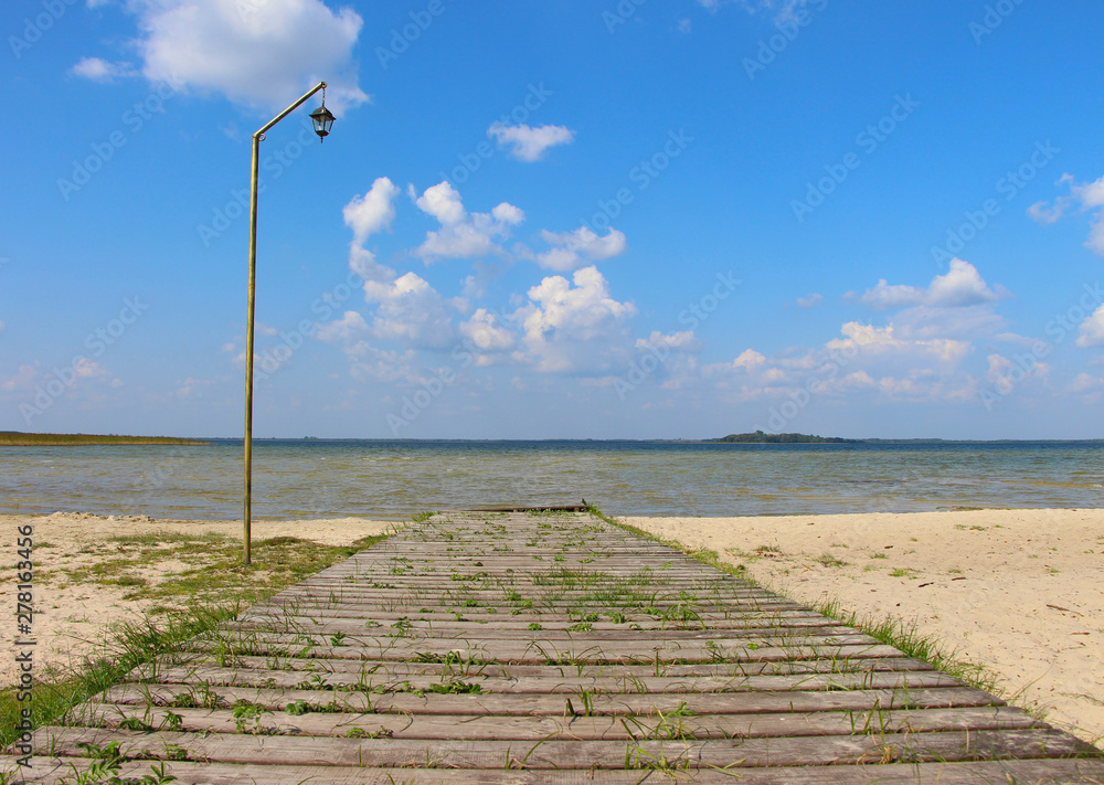 Wooden old ferny pier with vintage lamppost near the lake against blue summer sky
