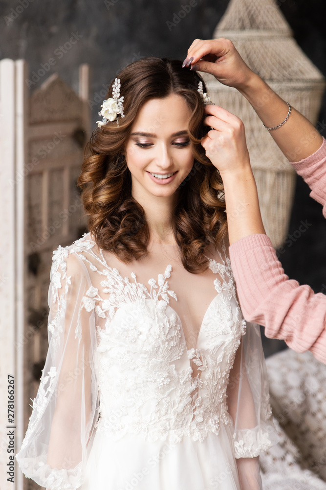 Hair stylist makes hair the bride. Portrait romantic bride with beautiful hairstyle. Luxurious white wedding dress. Elegant hair accessorie. Hair stylist makes hair the bride. Portrait romantic bride with beautiful hairstyle. Luxurious white wedding dress. Elegant hair accessorie.