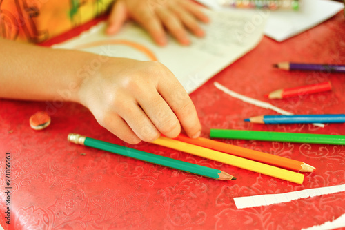 Young girl drawing with colored pencils, she is choosing a pencil in a pen holder, creativity and childhood concept.